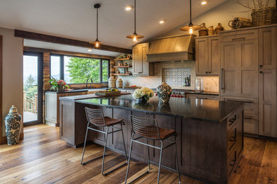 Mid-sized transitional l-shaped medium tone wood floor and brown floor kitchen photo in Portland with a farmhouse sink, shaker cabinets, medium tone wood cabinets, soapstone countertops, beige backsplash, porcelain backsplash, stainless steel appliances and an island