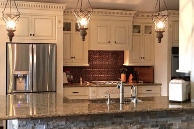 Example of a mid-sized transitional limestone floor eat-in kitchen design in Houston with a drop-in sink, raised-panel cabinets, distressed cabinets, granite countertops, metallic backsplash, stainless steel appliances and a peninsula