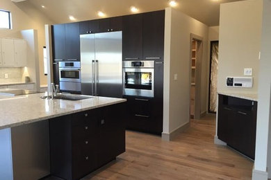 Example of a large trendy light wood floor and gray floor eat-in kitchen design in Other with an undermount sink, flat-panel cabinets, dark wood cabinets, quartz countertops, white backsplash, ceramic backsplash, stainless steel appliances and an island