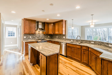 Example of a mid-sized classic u-shaped light wood floor enclosed kitchen design in New York with a double-bowl sink, shaker cabinets, medium tone wood cabinets, granite countertops, gray backsplash, matchstick tile backsplash, stainless steel appliances and an island