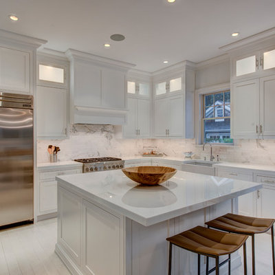 Mid-sized elegant l-shaped painted wood floor eat-in kitchen photo in New York with a farmhouse sink, recessed-panel cabinets, white cabinets, white backsplash, stainless steel appliances, an island, solid surface countertops, stone tile backsplash and white countertops