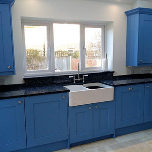 Klassische Küche mit Landhausspüle, blauen Schränken, Granit-Arbeitsplatte, weißen Elektrogeräten, Travertin und beigem Boden in Dorset