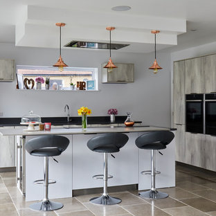 Photo of a large contemporary kitchen in London with flat-panel cabinets, grey cabinets, an island, black appliances, grey floors and black worktops.