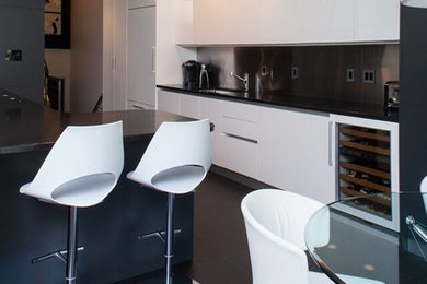 Modern inredning av ett kök, med släta luckor, vita skåp, bänkskiva i kvarts, stänkskydd med metallisk yta, integrerade vitvaror, klinkergolv i keramik och en halv köksö