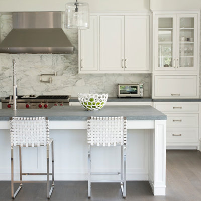 Eat-in kitchen - mid-sized transitional galley medium tone wood floor and gray floor eat-in kitchen idea in New York with recessed-panel cabinets, white cabinets, gray backsplash, stainless steel appliances, an island, marble backsplash, a farmhouse sink and quartz countertops