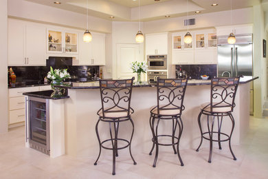 Photo of a large contemporary l-shaped kitchen in Phoenix with white cabinets, marble worktops, black splashback, stainless steel appliances, travertine flooring and an island.