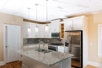 Mid-sized elegant l-shaped light wood floor kitchen photo in Atlanta with a double-bowl sink, raised-panel cabinets, white cabinets, granite countertops, mirror backsplash, stainless steel appliances and an island