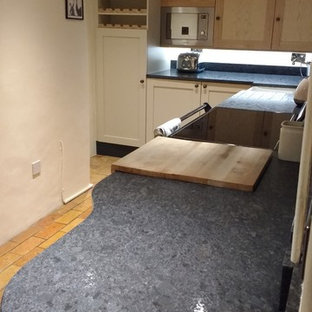 This is an example of a small eclectic l-shaped eat-in kitchen in Other with a farmhouse sink, shaker cabinets, granite benchtops, black splashback, stone slab splashback, coloured appliances, brick floors and no island.