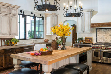 Inspiration for a large mediterranean u-shaped medium tone wood floor and brown floor open concept kitchen remodel in Phoenix with a farmhouse sink, raised-panel cabinets, distressed cabinets, concrete countertops, white backsplash, terra-cotta backsplash, stainless steel appliances, an island and brown countertops