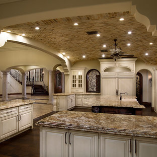 This is an example of an expansive mediterranean u-shaped separate kitchen in Phoenix with a farmhouse sink, louvered cabinets, white cabinets, granite benchtops, beige splashback, mosaic tile splashback, panelled appliances, dark hardwood floors and multiple islands.