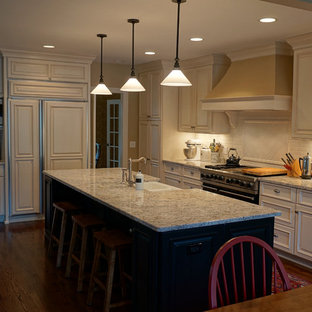 Mid-sized traditional eat-in kitchen photos - Mid-sized elegant l-shaped medium tone wood floor eat-in kitchen photo in Chicago with a farmhouse sink, raised-panel cabinets, white cabinets, granite countertops, white backsplash, subway tile backsplash, stainless steel appliances and an island