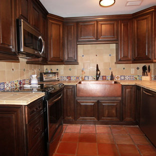 Esempio di una cucina rustica di medie dimensioni con lavello stile country, ante con bugna sagomata, ante in legno scuro, top piastrellato, paraspruzzi beige, paraspruzzi con piastrelle in ceramica, elettrodomestici in acciaio inossidabile e pavimento in terracotta