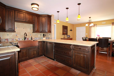 Example of a mid-sized mountain style u-shaped terra-cotta tile eat-in kitchen design in Tampa with a farmhouse sink, raised-panel cabinets, medium tone wood cabinets, tile countertops, beige backsplash, ceramic backsplash and stainless steel appliances