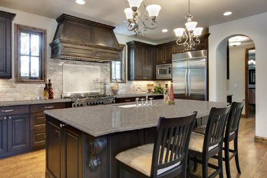 Eat-in kitchen - mid-sized traditional l-shaped light wood floor and brown floor eat-in kitchen idea in Other with raised-panel cabinets, dark wood cabinets, granite countertops, beige backsplash, subway tile backsplash, stainless steel appliances and an island
