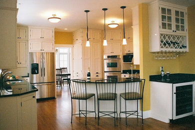 ワシントンD.C.にある高級な中くらいなトラディショナルスタイルのおしゃれなキッチン (アンダーカウンターシンク、フラットパネル扉のキャビネット、白いキャビネット、御影石カウンター、シルバーの調理設備、ラミネートの床、茶色い床、青いキッチンカウンター) の写真