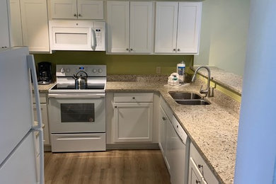Example of a small transitional l-shaped medium tone wood floor and brown floor eat-in kitchen design in Atlanta with a double-bowl sink, shaker cabinets, white cabinets, granite countertops, white appliances and no island