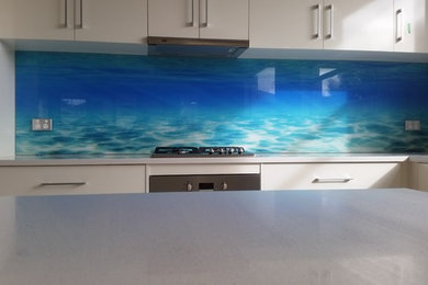 Imagen de cocina lineal costera con salpicadero azul y salpicadero de vidrio templado