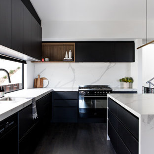 Contemporary l-shaped kitchen in Wollongong with a double-bowl sink, flat-panel cabinets, black cabinets, white splashback, panelled appliances, painted wood floors, with island, black floor and white benchtop.