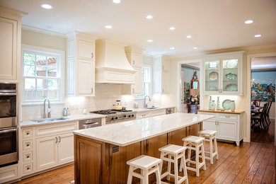 Example of a large transitional u-shaped brown floor and medium tone wood floor eat-in kitchen design in New Orleans with an island, an undermount sink, recessed-panel cabinets, white cabinets, white backsplash, subway tile backsplash, stainless steel appliances, white countertops and quartzite countertops