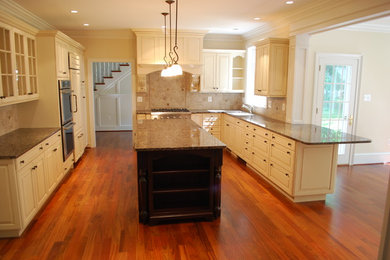 Eat-in kitchen - large traditional u-shaped medium tone wood floor and brown floor eat-in kitchen idea in Philadelphia with an undermount sink, raised-panel cabinets, white cabinets, beige backsplash, stainless steel appliances and an island