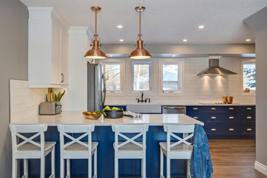 Eat-in kitchen - mid-sized transitional l-shaped vinyl floor and brown floor eat-in kitchen idea in Edmonton with a farmhouse sink, shaker cabinets, blue cabinets, quartz countertops, white backsplash, porcelain backsplash, stainless steel appliances and white countertops