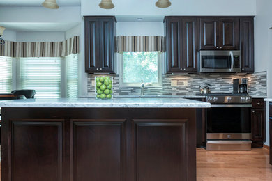 Exempel på ett mellanstort klassiskt grå grått kök, med en dubbel diskho, luckor med upphöjd panel, skåp i mörkt trä, bänkskiva i kvarts, grått stänkskydd, stänkskydd i stickkakel, rostfria vitvaror, mellanmörkt trägolv, en köksö och brunt golv