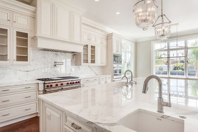 Mid-sized transitional l-shaped medium tone wood floor and brown floor eat-in kitchen photo in Tampa with an undermount sink, raised-panel cabinets, white cabinets, marble countertops, white backsplash, marble backsplash, stainless steel appliances and an island