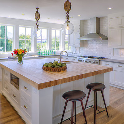 Example of a farmhouse u-shaped medium tone wood floor kitchen design in San Francisco with an undermount sink, shaker cabinets, white cabinets, white backsplash, subway tile backsplash, stainless steel appliances and an island