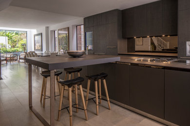 This is an example of a medium sized contemporary single-wall open plan kitchen in London with flat-panel cabinets, brown cabinets, metallic splashback, mirror splashback, stainless steel appliances, an island and grey floors.
