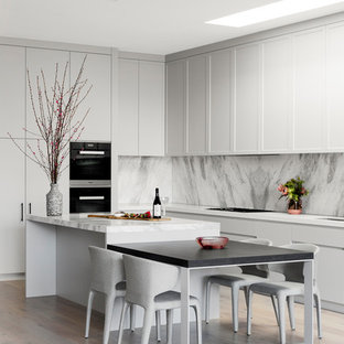Design ideas for a contemporary l-shaped kitchen in Melbourne with shaker cabinets, white cabinets, grey splashback, stone slab splashback, black appliances, light hardwood floors, with island, beige floor and white benchtop.