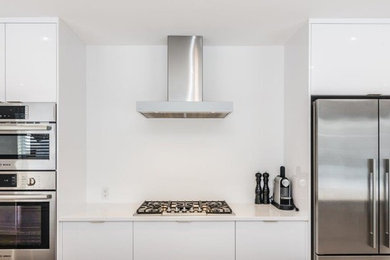 Eat-in kitchen - large contemporary single-wall light wood floor eat-in kitchen idea in Montreal with an undermount sink, flat-panel cabinets, white cabinets, quartzite countertops, white backsplash, stainless steel appliances and an island