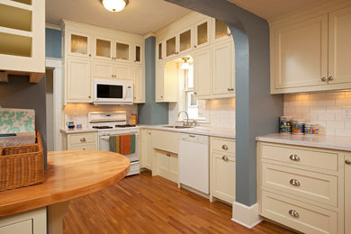ミネアポリスにある高級な中くらいなトラディショナルスタイルのおしゃれなキッチン (アンダーカウンターシンク、落し込みパネル扉のキャビネット、白いキャビネット、大理石カウンター、白いキッチンパネル、サブウェイタイルのキッチンパネル、白い調理設備、淡色無垢フローリング、アイランドなし、ベージュの床) の写真