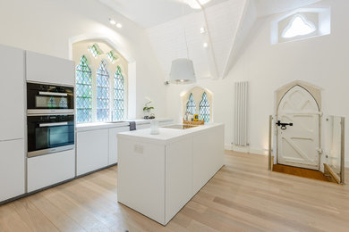 This is an example of a medium sized eclectic single-wall open plan kitchen in Hampshire with a submerged sink, flat-panel cabinets, white cabinets, an island, beige floors, white worktops and light hardwood flooring.