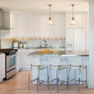 Inspiration for a beach style l-shaped kitchen in Portland Maine with an integrated sink, flat-panel cabinets, white cabinets, stainless steel benchtops, white appliances, grey splashback and mosaic tile splashback.
