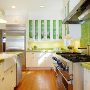 This is an example of a traditional kitchen in Calgary with stainless steel appliances, a belfast sink, tile countertops, glass-front cabinets, white cabinets, green splashback and green worktops.