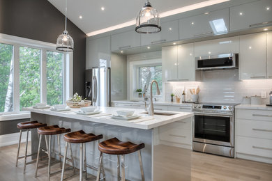 Example of a trendy galley light wood floor and beige floor kitchen design in Toronto with an undermount sink, flat-panel cabinets, white cabinets, white backsplash, stainless steel appliances, an island and white countertops