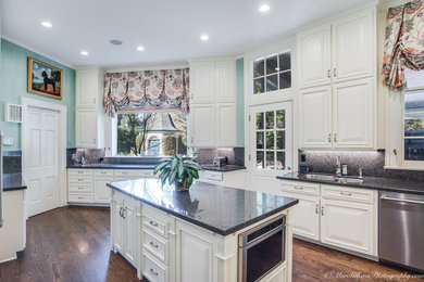 Klassisk inredning av ett stort u-kök, med en undermonterad diskho, luckor med upphöjd panel, vita skåp, granitbänkskiva, flerfärgad stänkskydd, stänkskydd i sten, rostfria vitvaror, mellanmörkt trägolv och en köksö