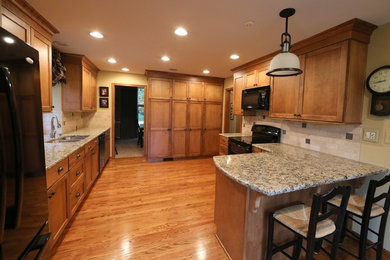 Example of a large transitional u-shaped medium tone wood floor and brown floor eat-in kitchen design in Kansas City with an undermount sink, granite countertops, beige backsplash, stone tile backsplash, black appliances, shaker cabinets, medium tone wood cabinets and a peninsula