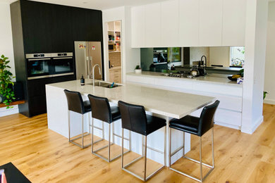Modern inredning av ett mellanstort beige beige kök, med en integrerad diskho, släta luckor, vita skåp, bänkskiva i kvarts, stänkskydd med metallisk yta, spegel som stänkskydd, rostfria vitvaror, ljust trägolv, en köksö och gult golv