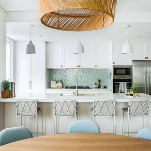 This is an example of a beach style eat-in kitchen in Wollongong with shaker cabinets, white cabinets, green splashback, stainless steel appliances, medium hardwood floors, with island and white benchtop.