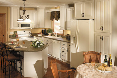 Example of a mid-sized classic l-shaped medium tone wood floor eat-in kitchen design in Chicago with a drop-in sink, raised-panel cabinets, white cabinets, white appliances and an island