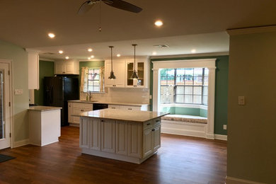 Photo of a large traditional galley open plan kitchen in New Orleans with raised-panel cabinets, white cabinets, an island, granite worktops, a submerged sink, white splashback, metro tiled splashback, black appliances, medium hardwood flooring, brown floors and beige worktops.