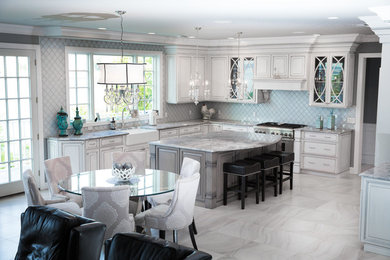 Large transitional l-shaped porcelain tile eat-in kitchen photo in New York with a farmhouse sink, raised-panel cabinets, white cabinets, granite countertops, white backsplash, ceramic backsplash, stainless steel appliances and an island