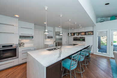 Example of a mid-sized trendy galley medium tone wood floor kitchen design in DC Metro with an undermount sink, flat-panel cabinets, white cabinets, marble countertops, white backsplash, stone tile backsplash, stainless steel appliances and an island