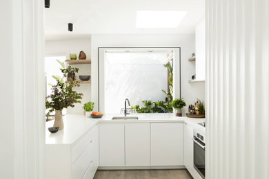 This is an example of a medium sized contemporary u-shaped open plan kitchen in Melbourne with a submerged sink, flat-panel cabinets, white cabinets, engineered stone countertops, grey splashback, stone slab splashback, stainless steel appliances, medium hardwood flooring, a breakfast bar, brown floors and white worktops.