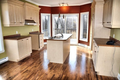 Eat-in kitchen - large traditional galley medium tone wood floor and brown floor eat-in kitchen idea in Montreal with laminate countertops, an island, a drop-in sink, raised-panel cabinets, white cabinets and brown countertops