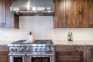 Bild på ett mellanstort amerikanskt kök, med skåp i shakerstil, skåp i mörkt trä, granitbänkskiva, vitt stänkskydd, stänkskydd i glaskakel, rostfria vitvaror, mellanmörkt trägolv, en undermonterad diskho och en köksö