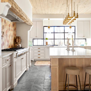 Cette photo montre une grand cuisine nature en L avec un placard à porte shaker, des portes de placard blanches, un îlot central, une crédence multicolore, une crédence en carreau de terre cuite, un sol noir, un plan de travail blanc, un évier de ferme, un plan de travail en quartz modifié, un électroménager en acier inoxydable et un sol en ardoise.