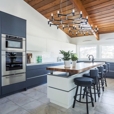 Inspiration for a mid-sized 1960s l-shaped ceramic tile and gray floor kitchen remodel in Other with flat-panel cabinets, blue cabinets, wood countertops, white backsplash, stainless steel appliances and an island