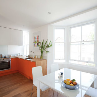 Offene, Kleine Moderne Küche ohne Insel in L-Form mit Unterbauwaschbecken, flächenbündigen Schrankfronten, orangefarbenen Schränken, Arbeitsplatte aus Holz, Küchenrückwand in Weiß, Glasrückwand, Küchengeräten aus Edelstahl und hellem Holzboden in London